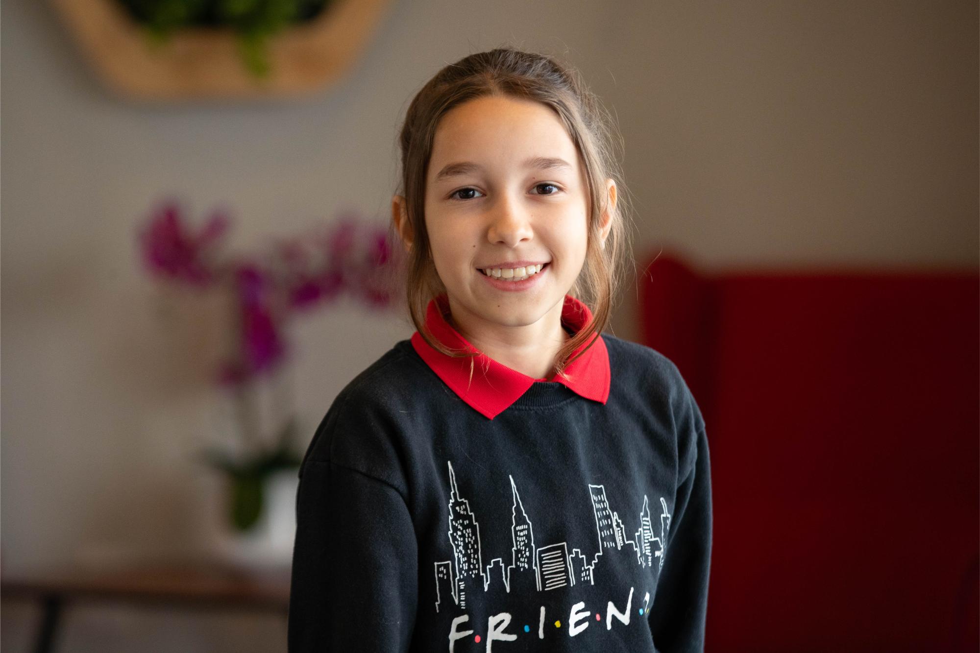 Smiling girl in a Friends-themed sweater, showcasing orthodontic care at Luv Braces, an Austin orthodontist.